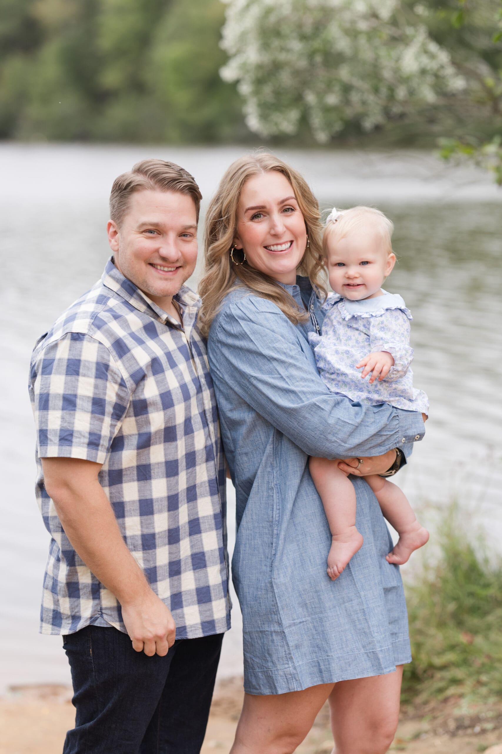 Family with 1 year old girl in blue tones smiles at the camera in Colonel Beatty Park in Matthews, NC